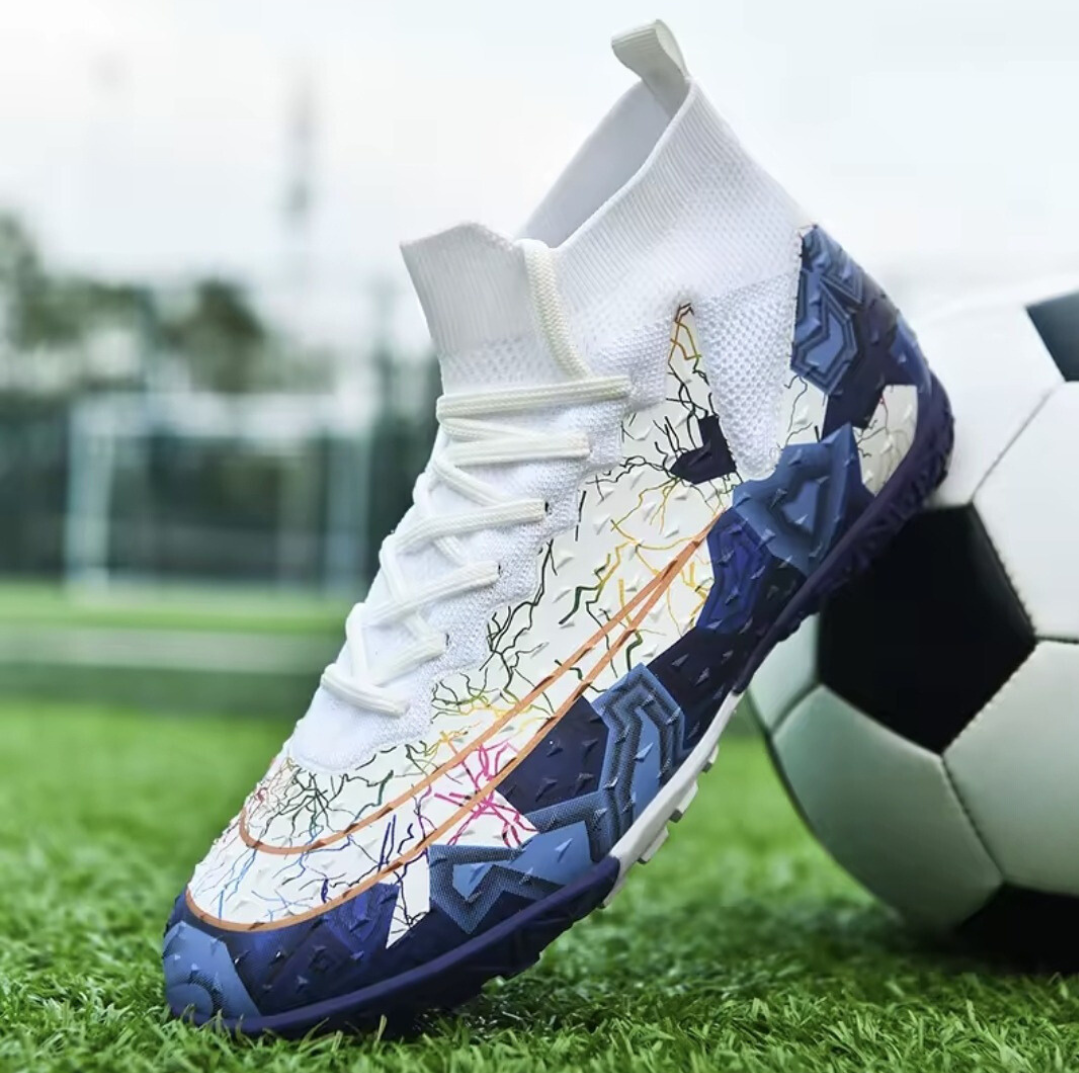 Tempesta Men’s Firm Ground Football Boots in white with blue sole and colourful crack details shown on a football pitch next to a ball