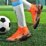 Tempesta Men’s Turf Football Boots in orange with black graphic details worn on artificial grass field with a football in the background