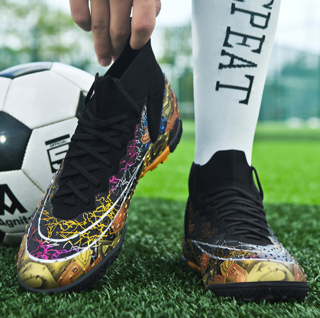Tempesta Men’s Turf Football Boots in black with gold graphic details worn on artificial grass field with a football in the background