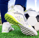 Galactic Men’s Turf Football Boot white patterned on foot next to a football on green artificial grass field background
