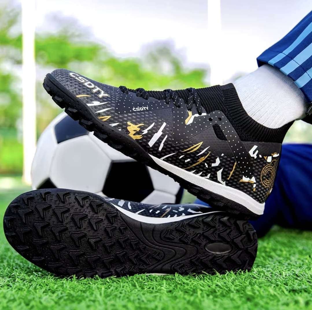 Galactic Men’s Turf Football Boot black patterned on foot next to a football on green artificial grass field background