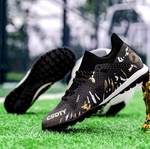 Pair of Galactic Men’s Turf Football Boots black patterned next to a football on green artificial grass field background
