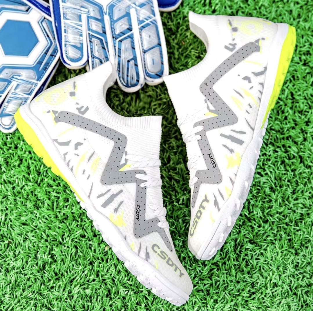 Pair of Galactic Men’s Turf Football Boots white patterned next to a football on green artificial grass field background