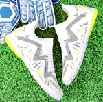 Pair of Galactic Men’s Turf Football Boots white patterned next to a football on green artificial grass field background