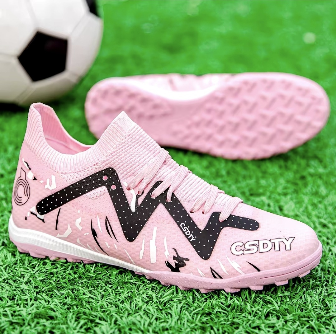 Pair of Galactic Men’s Turf Football Boots pink patterned next to a football on green artificial grass field background
