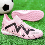 Pair of Galactic Men’s Turf Football Boots pink patterned next to a football on green artificial grass field background