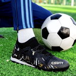 Galactic Men’s Turf Football Boot black patterned on foot next to a football on green artificial grass field background
