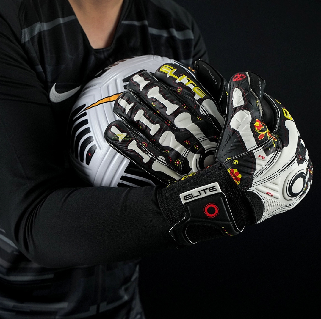 Goalkeeper holding football with Elite Sport Pro Calavera gloves featuring skeleton and floral details on black background