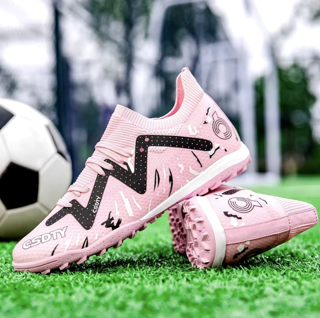 Pair of Galactic Men’s Turf Football Boots pink patterned next to a football on green artificial grass field background
