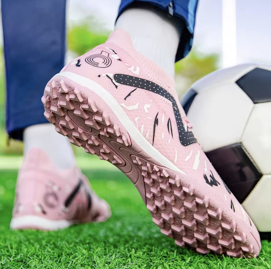 Galactic Men’s Turf Football Boot pink patterned on foot next to a football on green artificial grass field background