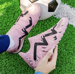 Galactic Men’s Turf Football Boot pink patterned on foot next to a football on green artificial grass field background