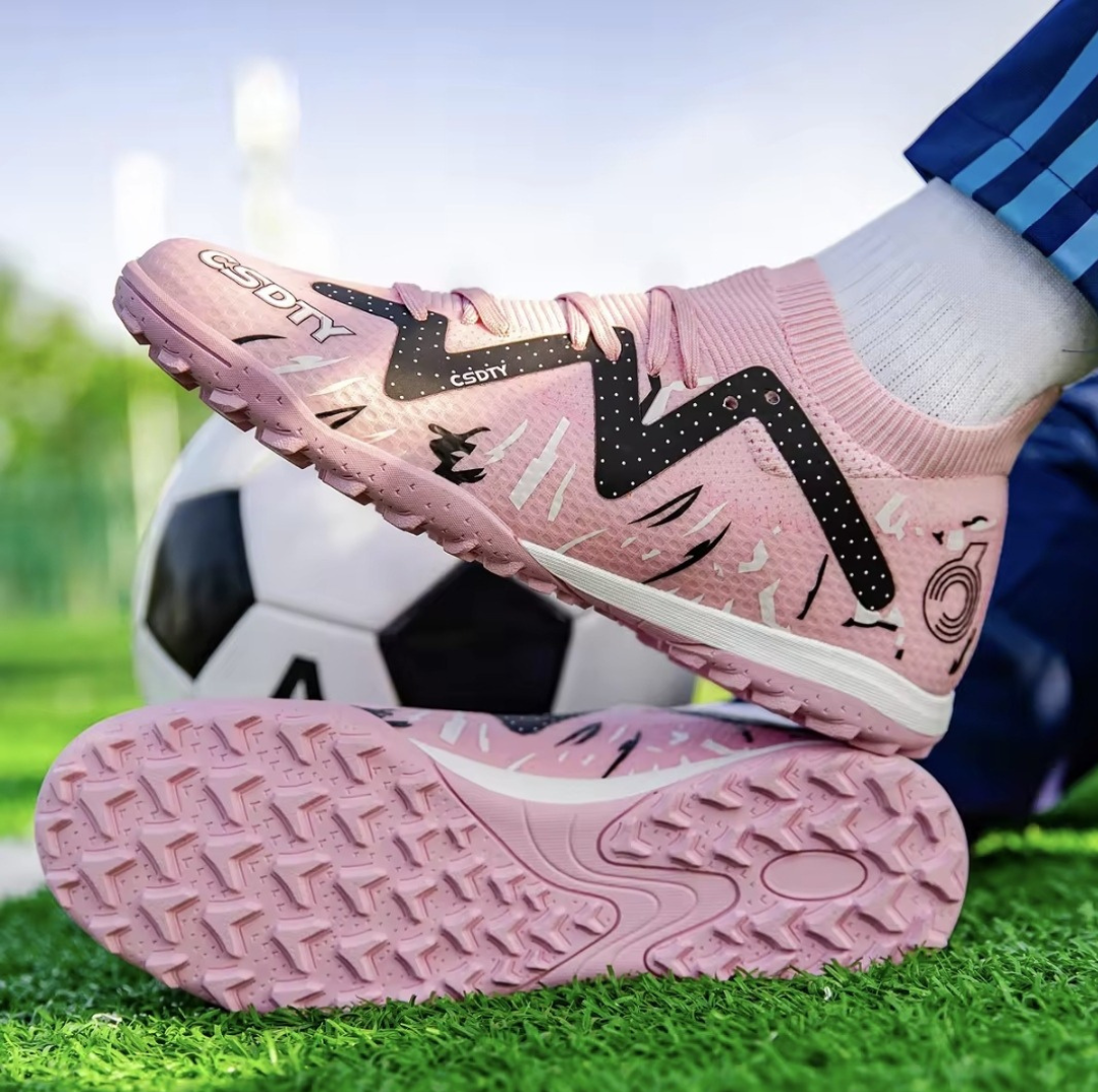 Galactic Men’s Turf Football Boot pink patterned on foot next to a football on green artificial grass field background