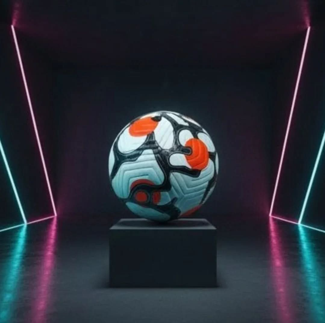 A football, predominantly white with black and orange panels, is displayed on a black plinth in a dark, futuristic room. The setting is illuminated by thin, vertical neon strip lights in bright pink and cyan, reflecting off the floor.