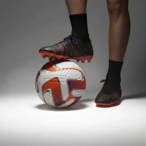 Football player standing with black and orange boots on the Vector ball, low-key studio lighting.