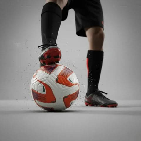 Football player standing with black and orange boots on the Vector ball, low-key studio lighting.