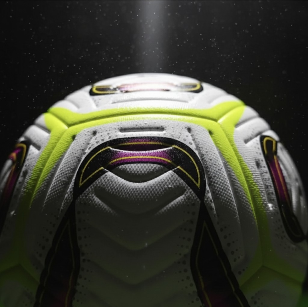 An extremely close-up view of the seamless textured surface of the Dynamo Football on a grassy pitch, highlighting the bright neon yellow and maroon/black graphical design.