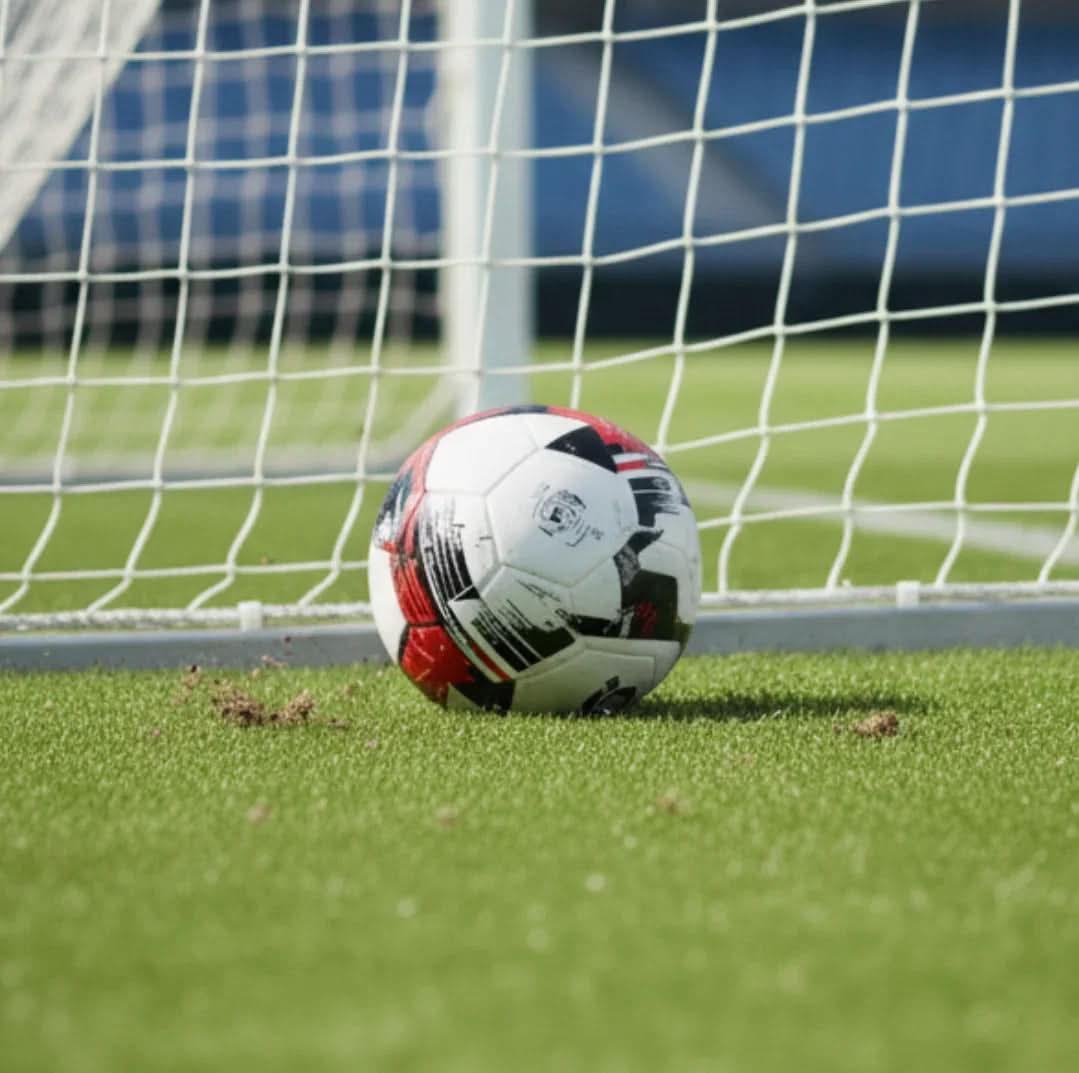 Football lying near the goal net on a green football field.