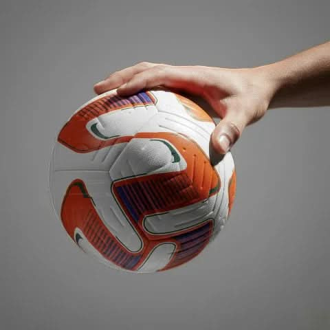 Hand holding the Vector football in mid-air, showcasing the orange and blue pattern detail.