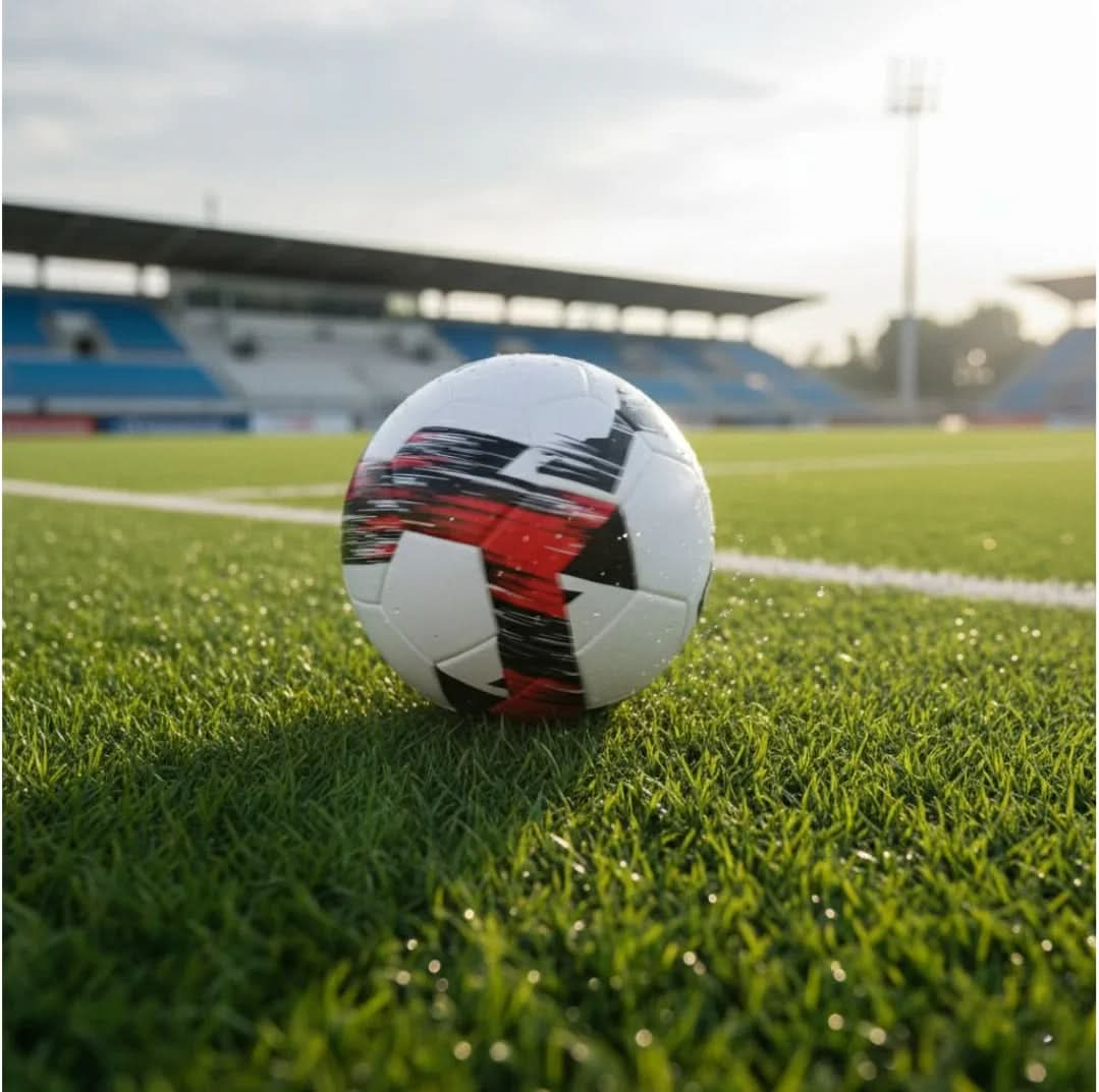 Football on a football pitch line with stadium and bright sky in the background.