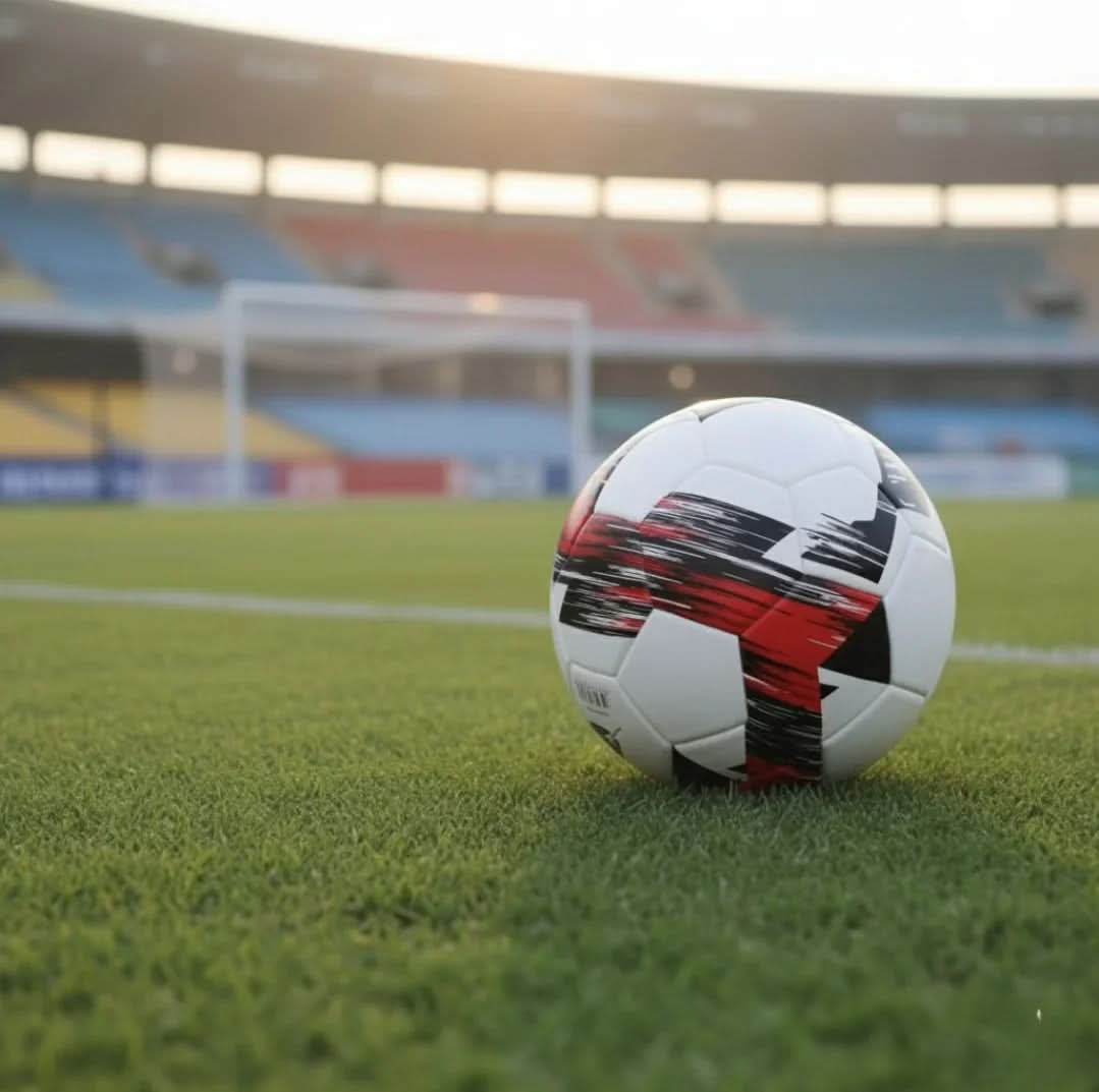 Close-up of a football on the grass pitch inside a stadium at sunset.